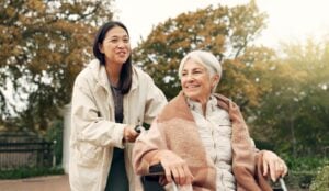 Woman in wheelchair in park with lady assisting her.
